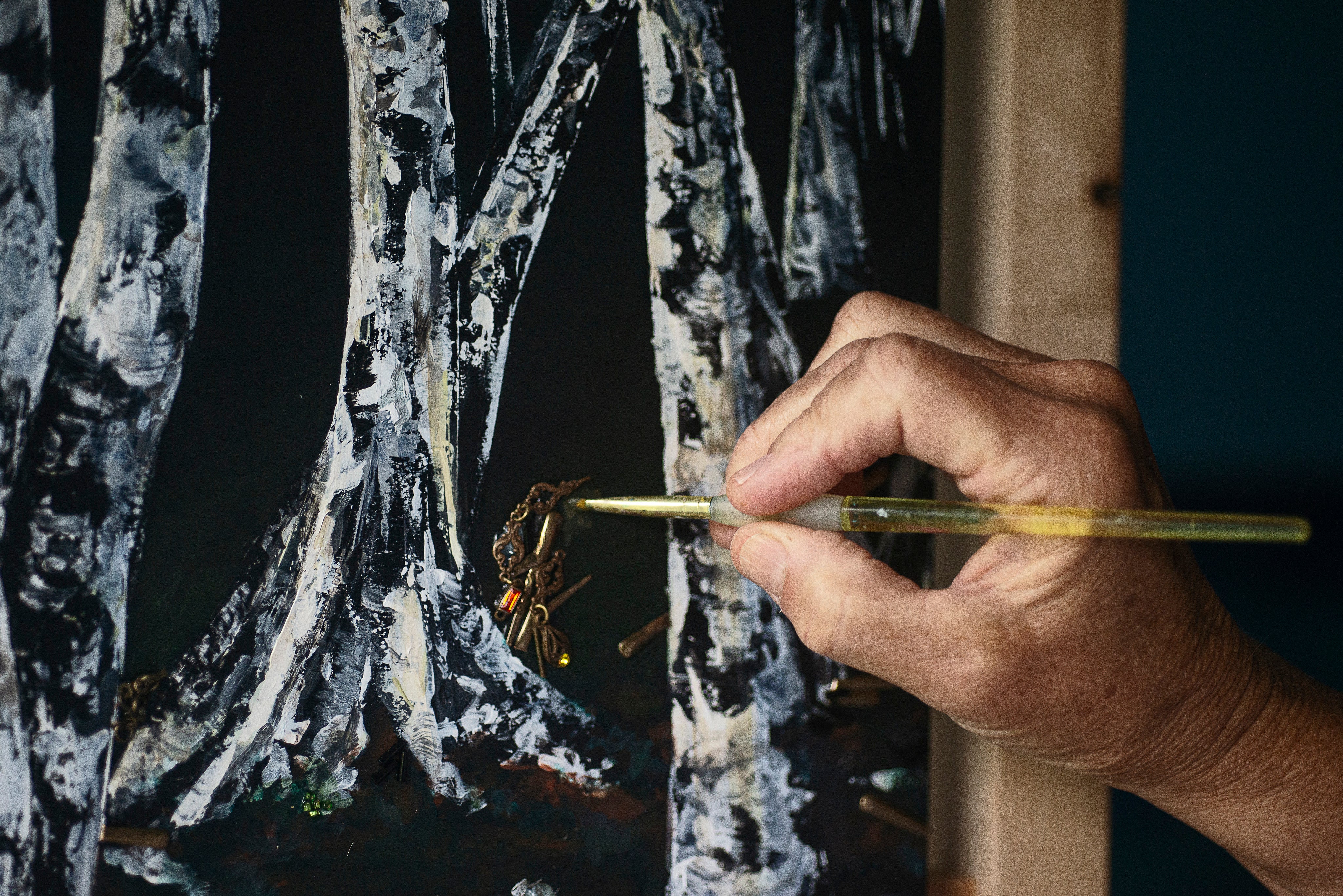 hand-holds-a-paint-brush-to-a-painting-of-birch-trees.jpg
